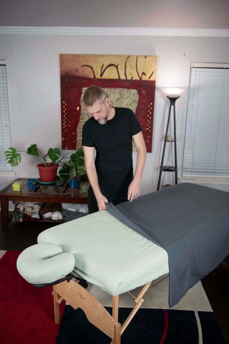 Practitioner assessing a client standing posture beside the treatment table